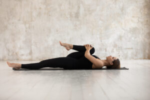 Woman wearing black sport clothes lying on floor with one knee pulled up to her chest.